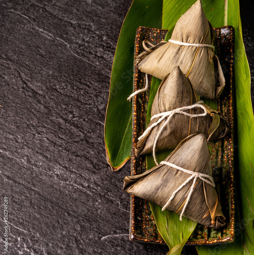 Close up, copy space, top view, flat lay. Famous asian chinese tasty handmade food in duan wu event, steamed rice dumplings shaped like pyramidal ingredient on black slate photo