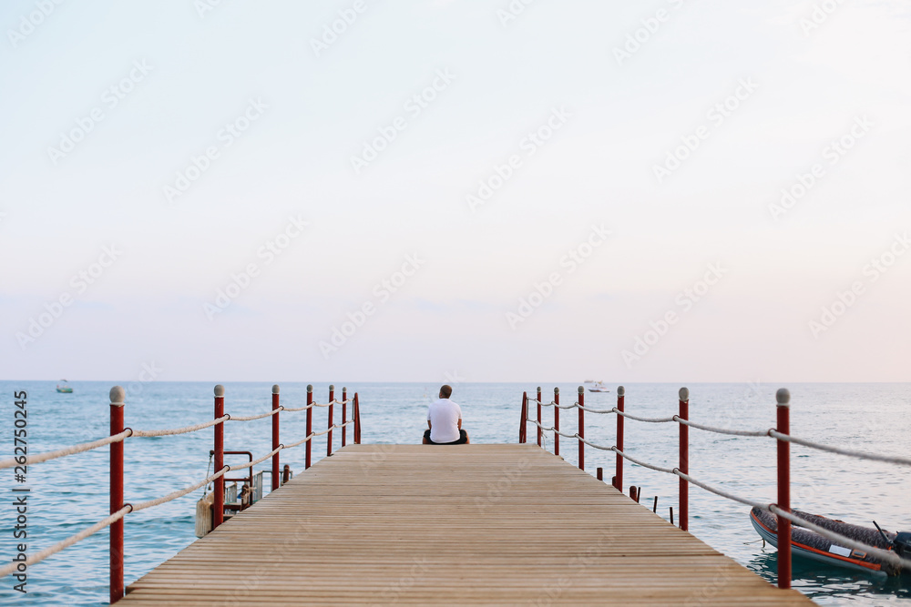 Man sitting on the pier and looking at the sea horizon and blue sky. Vacation at sea. Summer time sea vacation background 
