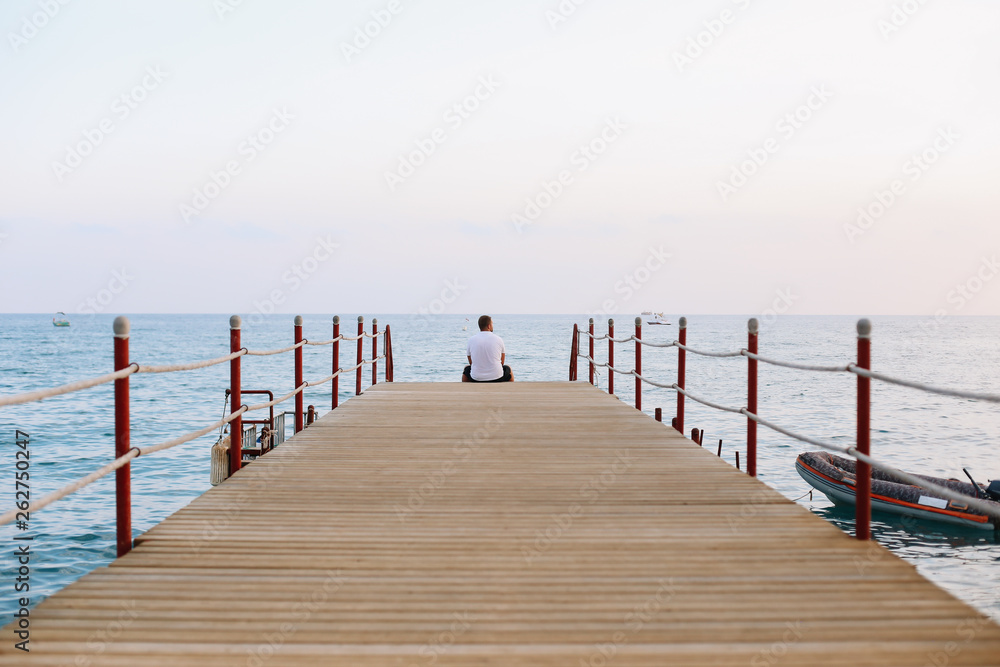 Man sitting on the pier and looking at the sea horizon and blue sky. Vacation at sea. Summer time sea vacation background 