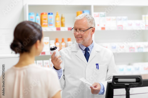 medicine, pharmaceutics, healthcare and people concept - senior apothecary with drug and prescription and female customer at pharmacy