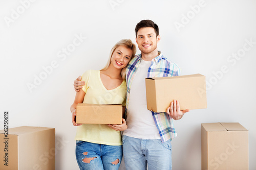 mortgage, moving, people and real estate concept - happy couple with big cardboard boxes at new home