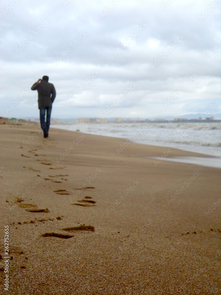 Silhouette of a man walking alone at the beach feeling lonely leaving footprints on the wet sand Silhouette of a man walking alone at the beach feeling lonely leaving footprints on the wet sand