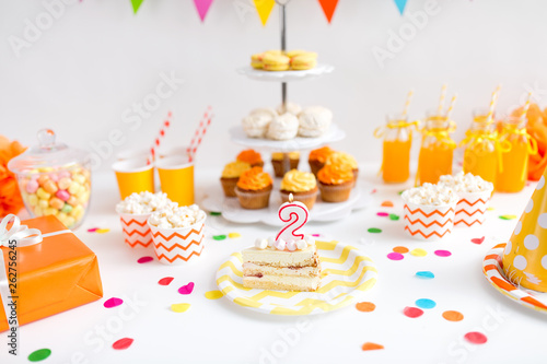 anniversary, celebration and festive concept - piece of cake with candle in shape of number two on plate at birthday party