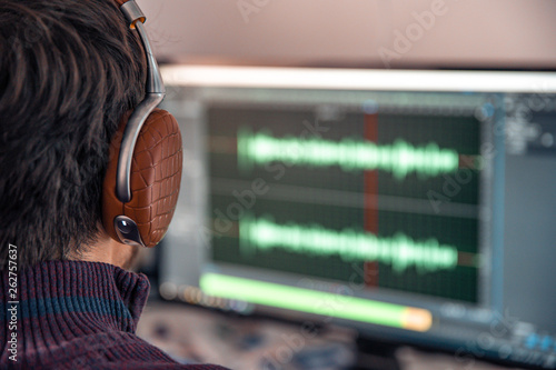 The man in the photo studio records and modifies singing, voice and music for commercial use. Works in an audio editor in a computer with headphone photo