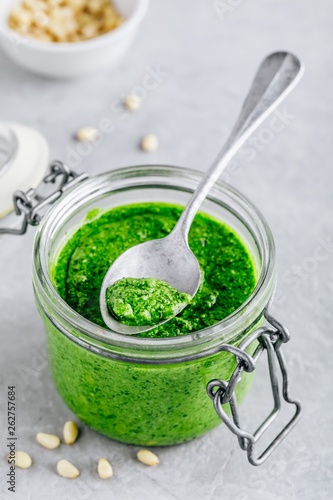 Homemade spinach pesto sauce in glass jar with parmesan cheese and olive oil