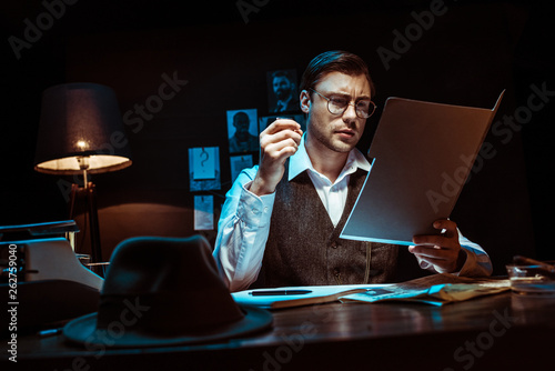 Cuadro en lienzo Concentrated detective in glasses reading dossier in dark office