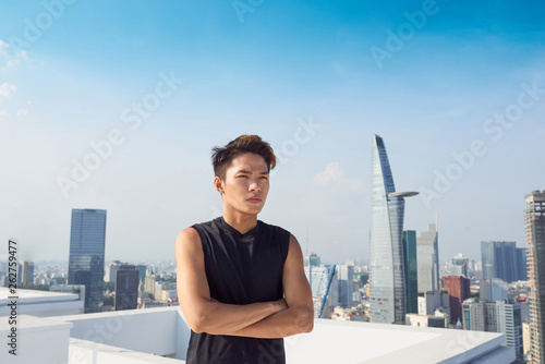Handsome asian man with sportswear standing on the background of the city crossing his arms