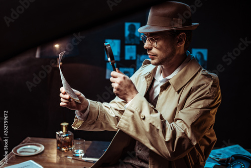 Fotografía Detective in trench coat looking at photo through magnifier