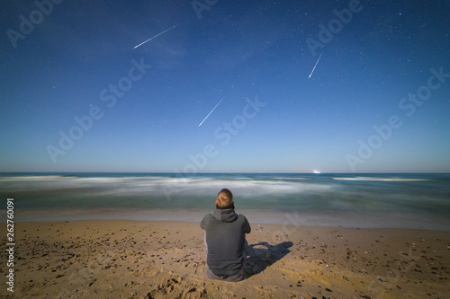 Young man on the Baltic seashore watching the meteor shower late at night