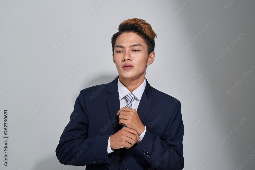 Confident businessman straightening his tie over gray background and looking at camera Confident businessman straightening his tie over gray background and looking at camera