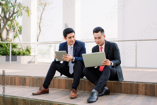 Canvas Print two asian business executives using ipad in city park.