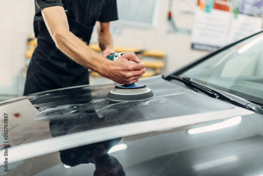 Male person with polishing machine cleans car hood