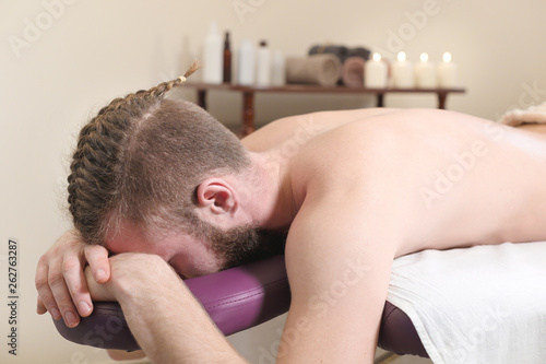 Male hipster with braided trendy hair and shaved temples lying on a massage bunk down face resting and waiting for physical therapy and massage