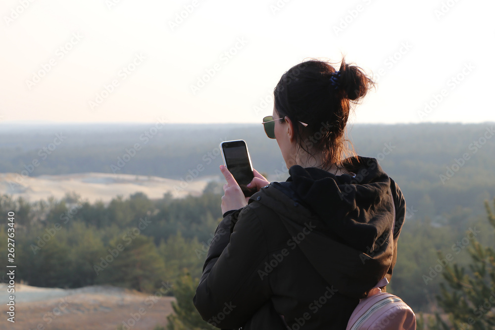 woman blogger photographing on the smartphone sand dunes during sunset and publishes in social network