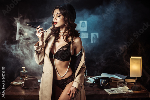 Sexy girl in black lingerie and trench coat holding mouthpiece in dark office