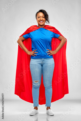 super power and people concept - happy african american young woman in superhero red cape over grey background
