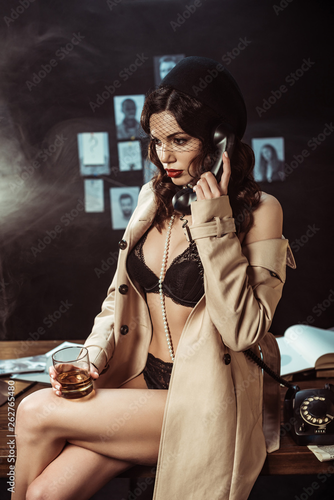Sexy woman in black lingerie and trench coat holding glass of cognac while  talking on telephone Photos | Adobe Stock