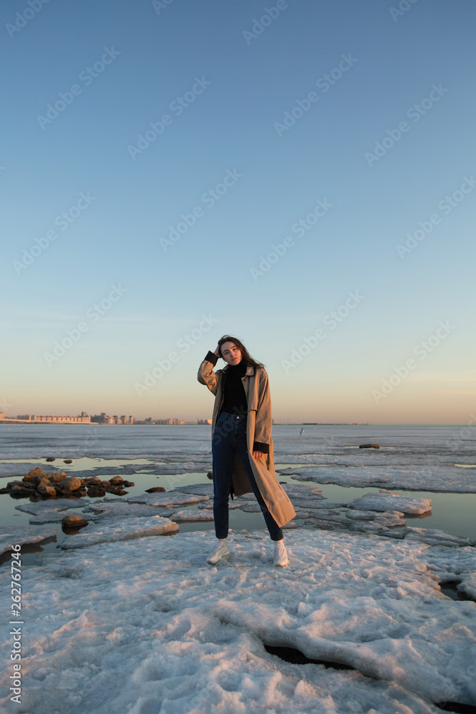 Charming young woman near the river with ice at spring.