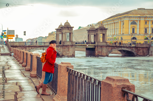 Blonde in a red coat walks along the embankment of the Fontanka River.