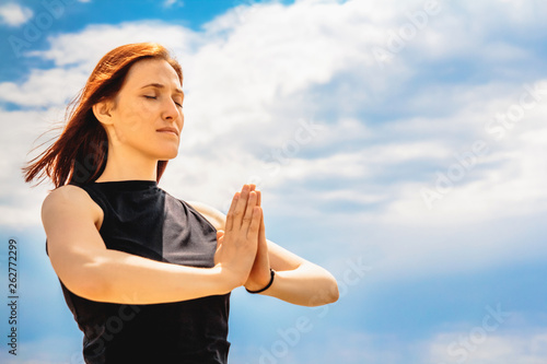 Portrait of attractive fitness woman relaxing yoga position against sky background