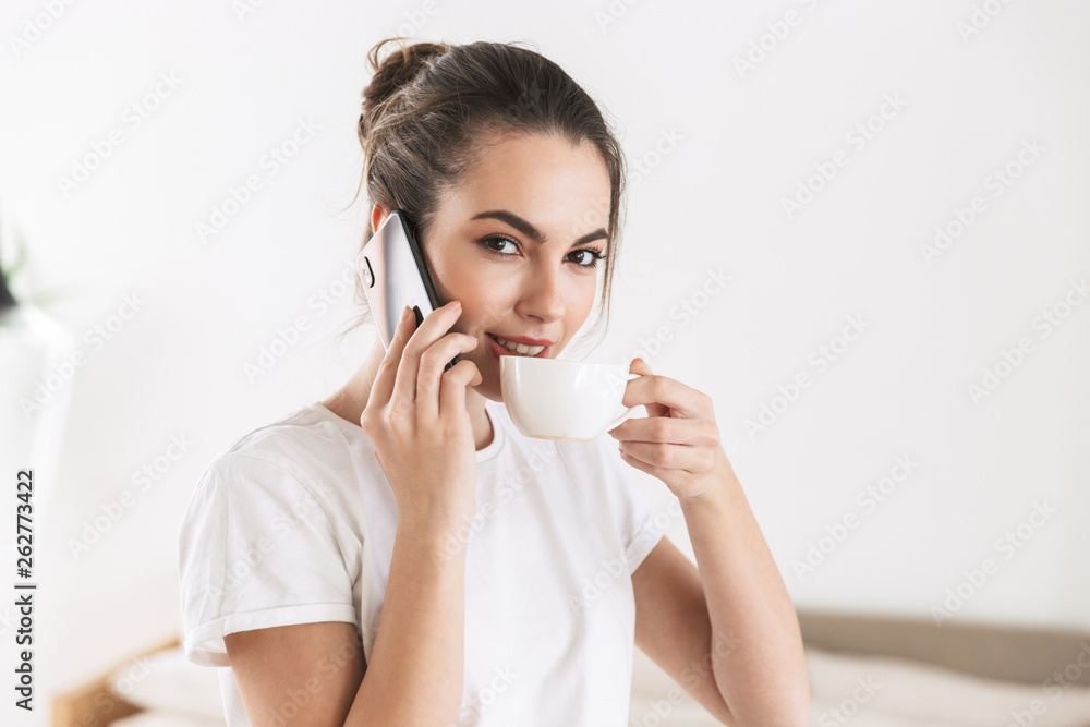 Student girl drinking coffee posing indoors talking by mobile phone. Student girl drinking coffee posing indoors talking by mobile phone.