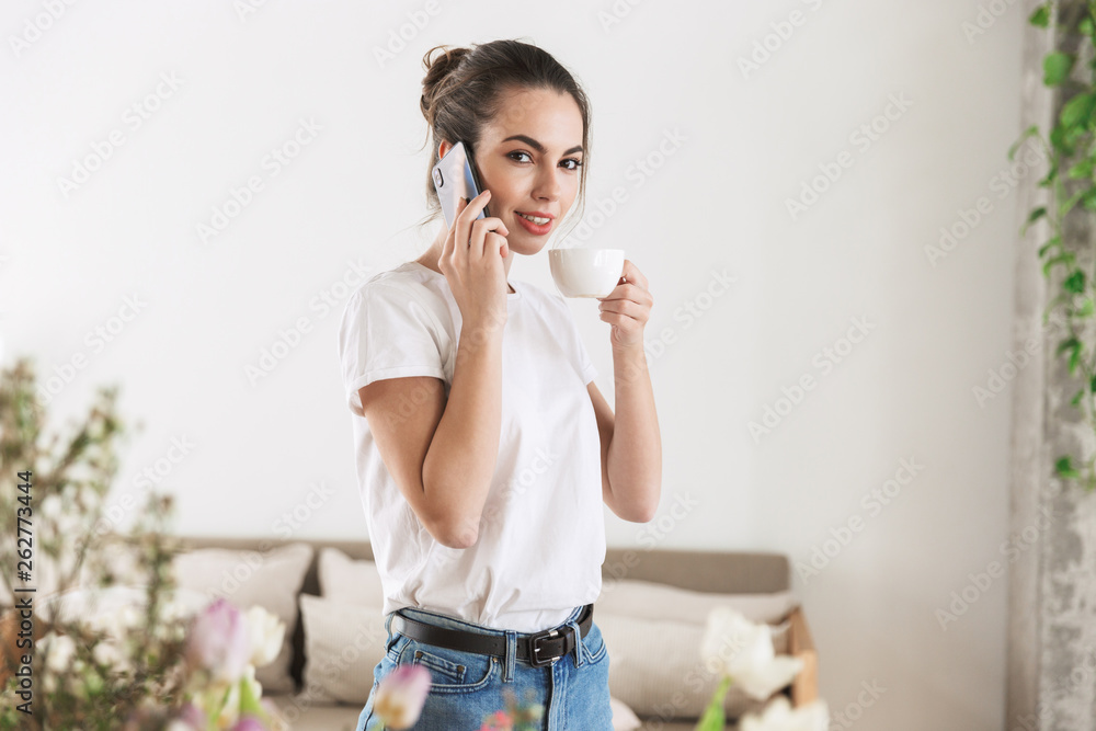 Student girl drinking coffee posing indoors talking by mobile phone. Student girl drinking coffee posing indoors talking by mobile phone.