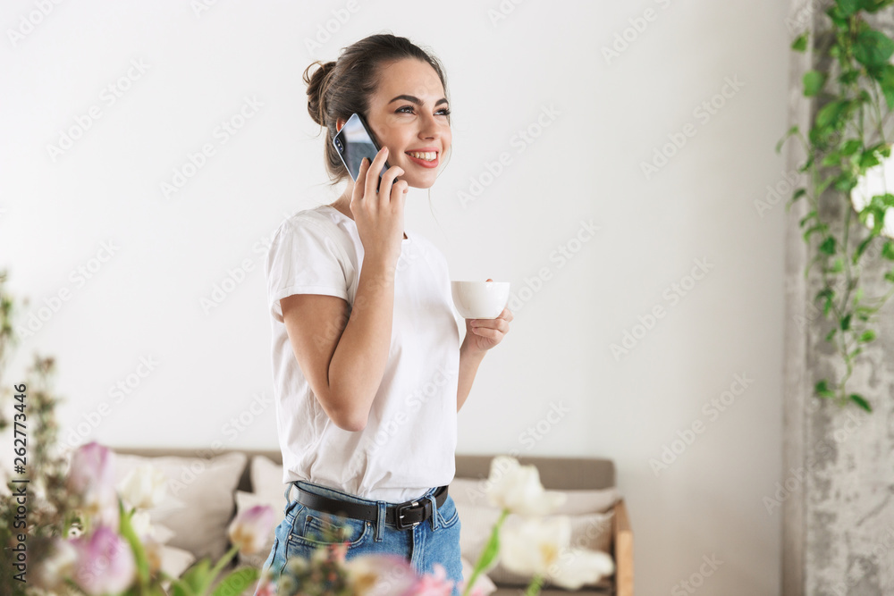 Student girl drinking coffee posing indoors talking by mobile phone. Student girl drinking coffee posing indoors talking by mobile phone.