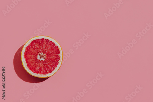 Fresh cutted grapefruit on a pastel pink background closeup at the left side of the table