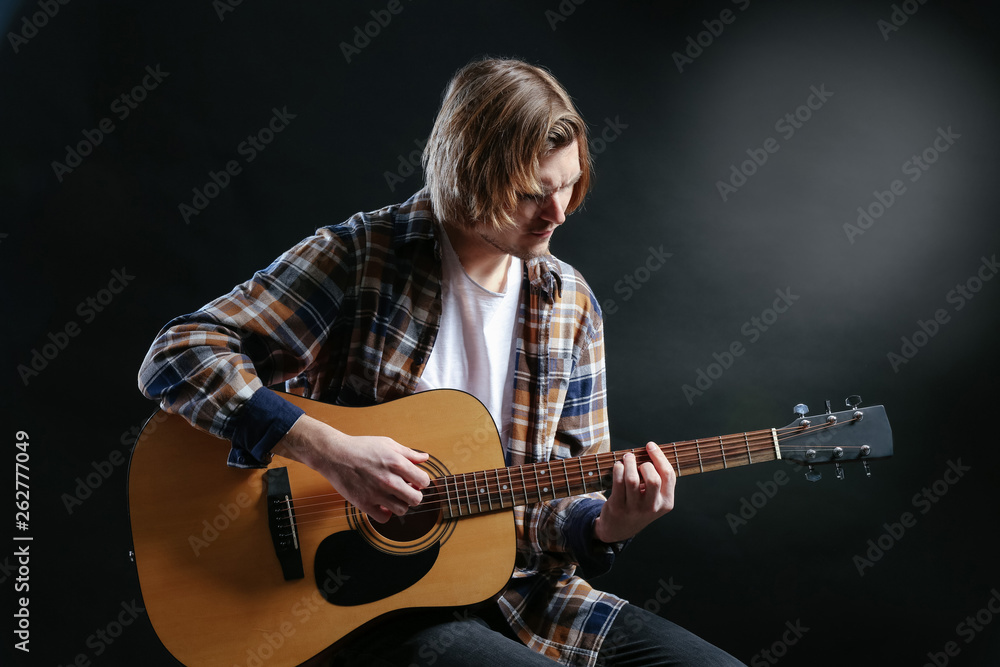 Obraz premium Handsome young man playing guitar on dark background