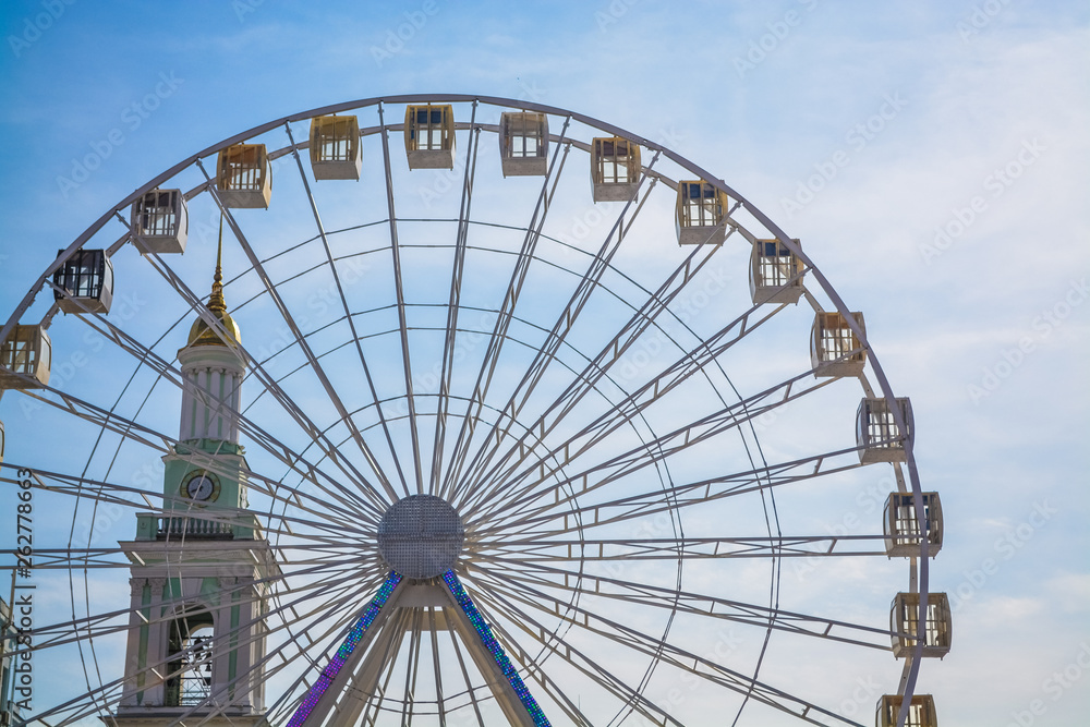 Big wheel against the background of the blue sky and an old city architecture Kiev, Ukraine. Amusement park. Area.