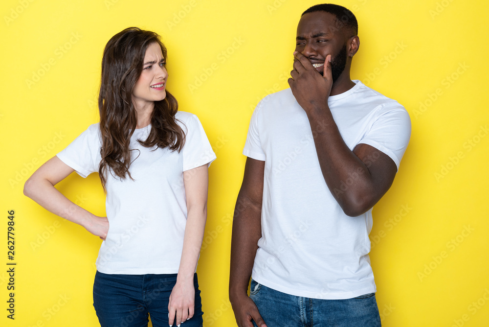Half length of squinting interracial couple in white T-shirts posing for camera