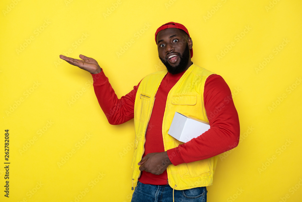 Half length of surprised African deliveryman keeping white box in arm Half length of surprised African deliveryman keeping white box in arm