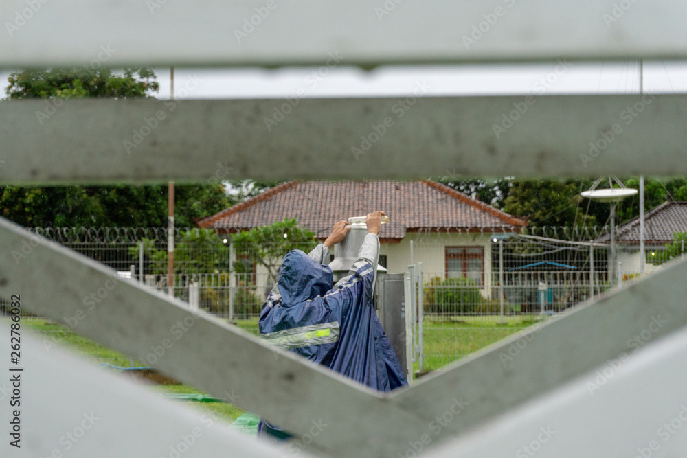 BALI/INDONESIA-DECEMBER 21 2017: A meteorological observer checks the Helman rain meter at meteorology garden to make sure this tool records and works well on rainy day BALI/INDONESIA-DECEMBER 21 2017: A meteorological observer checks the Helman rain meter at meteorology garden to make sure this tool records and works well on rainy day
