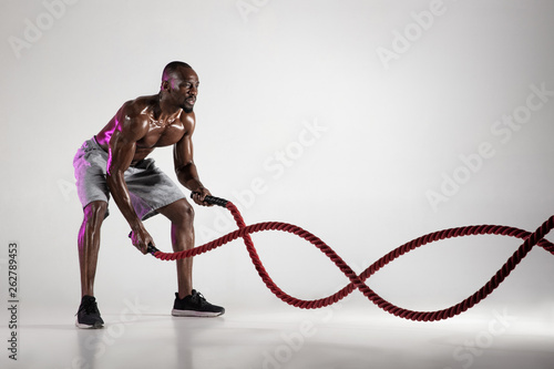 Young african-american bodybuilder training over grey background photo