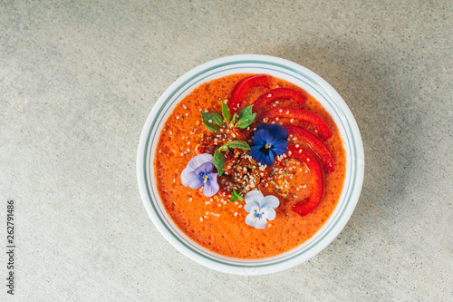 Tasty tomatoe soup in white bowl, decorated with little flowers, red bell pepper, hempseed and mint. Delicious meal. Vegetrian dish concept. Dinner time photo
