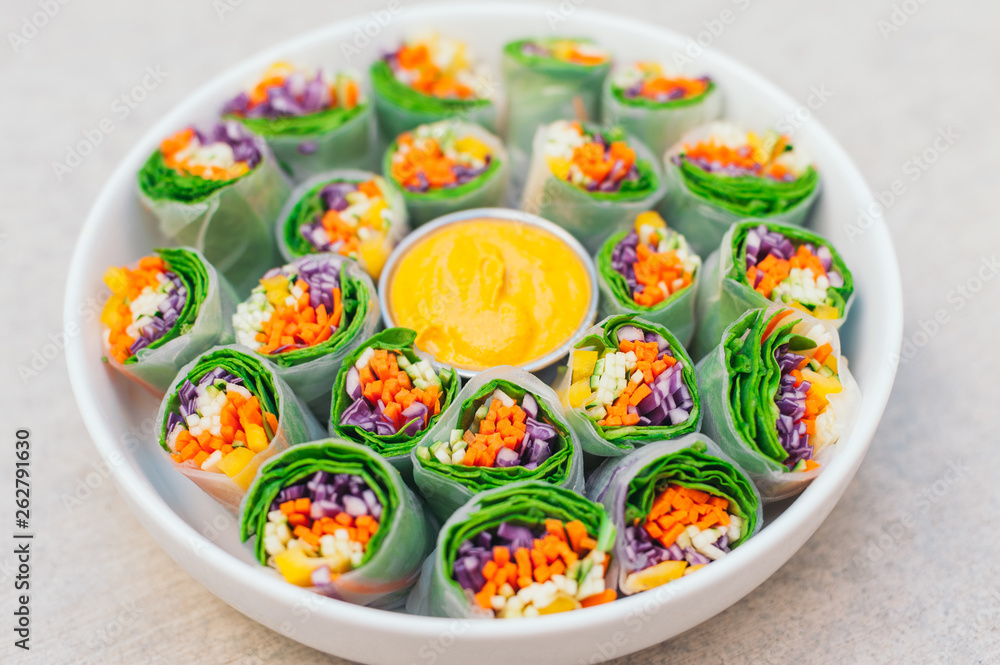 Vegan food concept. Tasty green spring rolls made of rice paper and spinach, filled with fresh chopped vegetables. Small plate with yellow curry sauce in middle