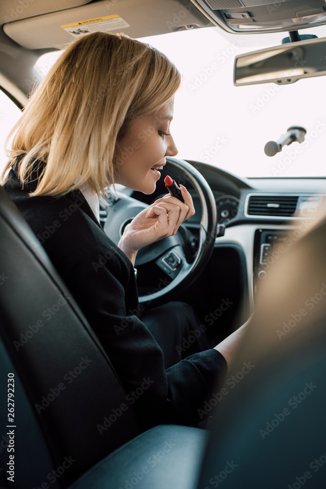 cheerful blonde girl applying lipstick while sitting in car cheerful blonde girl applying lipstick while sitting in car
