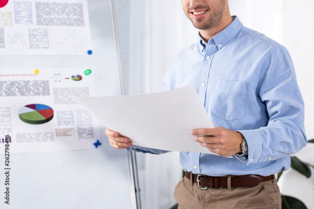 cropped view of cheerful businessman holding blank paper in office