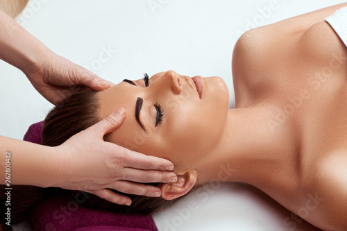Young beautiful woman enjoying anti-aging facial massage.Male therapist making head massage to female client.Professional masseur.Relaxation beauty spa body and face treatment concept.