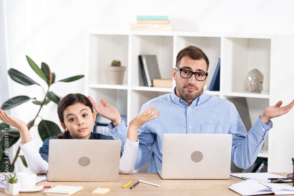handsome man in glasses and cute daughter gesturing near laptops