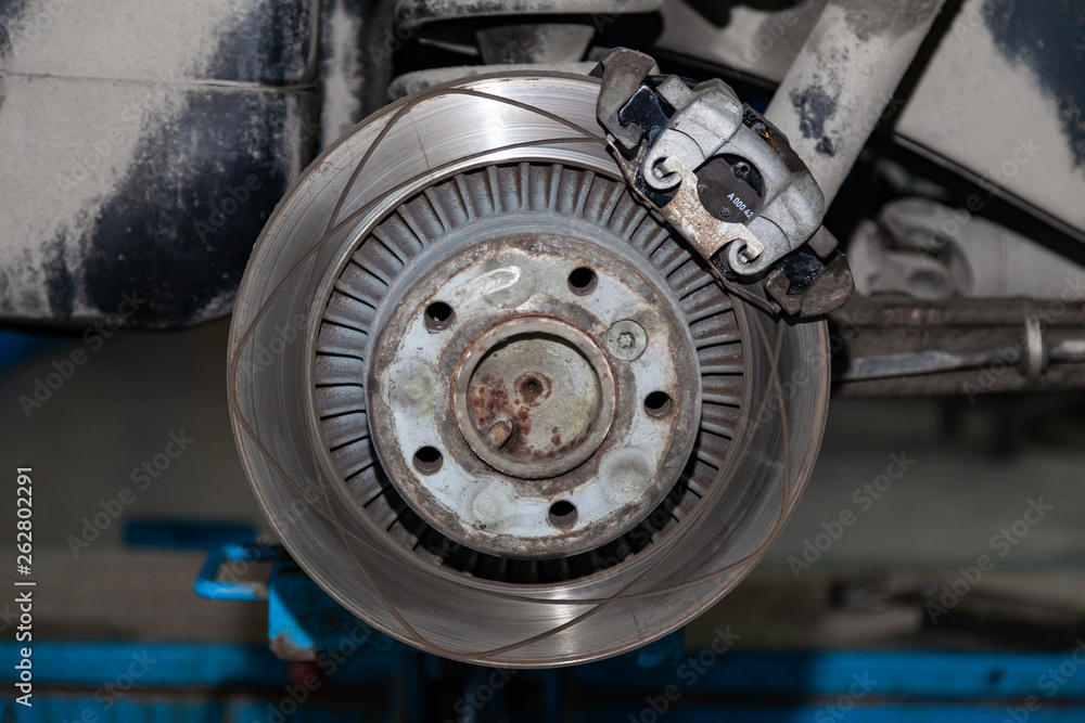 The braking system of the car with the wheel removed with the disc, pads, hub and cooling holes during maintenance and replacement in the workshop on the vehicle repair.