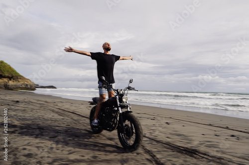 young man spread his arms on a motorcycle. ocean coast. freedom.