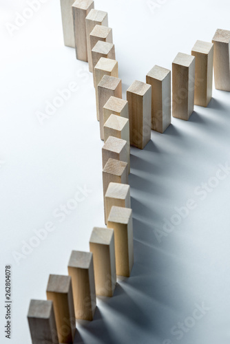 A long curved line of wooden cubes is divided into two  as a symbol of a queue  a competition for a position or a team  on an uneven white background. Vertical frame