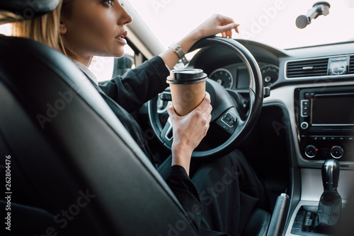 cropped view of blonde young woman holding paper cup while sitting in car © LIGHTFIELD STUDIOS