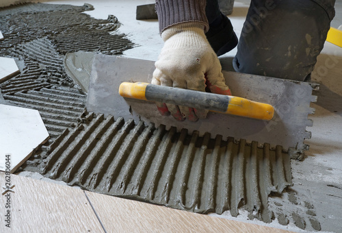 Fotografi The worker is putting tiles adhesive to the floor with the notched trowel