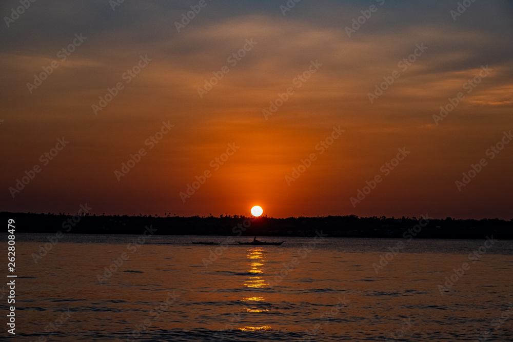 Silhouette image of a fisherman in the open sea as the sun sets behind an island.