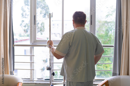 patient with a dropper looks out the window of the hospital room and smiles. back view. Healthcare concept.