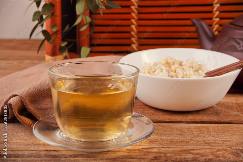 Cooked brown rice in white bowl with chopsticks and cup of green tea on the wooden background. Cooked brown rice in white bowl with chopsticks and cup of green tea on the wooden background.