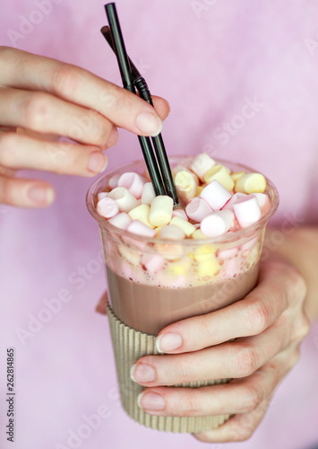 marshmallow cocoa in a disposable cup with two tubes in the hand of a woman