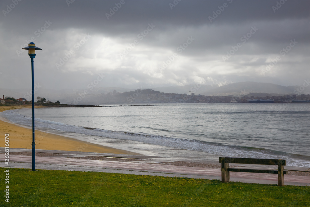 Lonely bench on the shore of the Atlantic Ocean, next to the lantern and a beautiful green lawn, Spain, mountain view, cloudy day